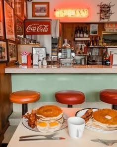 two breakfast plates with pancakes and eggs sit on a table in front of a bar