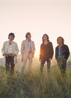 four people standing in tall grass on top of a hill with the sun behind them