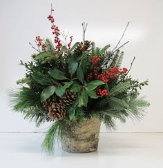 a potted plant with pine cones, berries and greenery on the top is sitting on a white surface