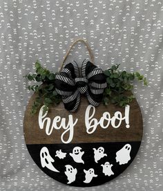 a wooden sign that says hey boo with ghost faces and black bow hanging on it