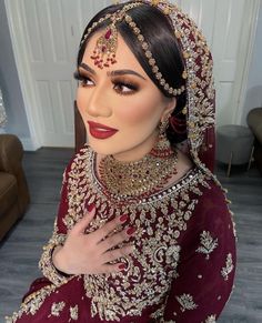 a woman wearing a red and gold bridal outfit with her hands on her chest