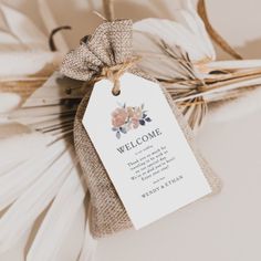 a welcome sign hanging from a burlock with flowers on it's side