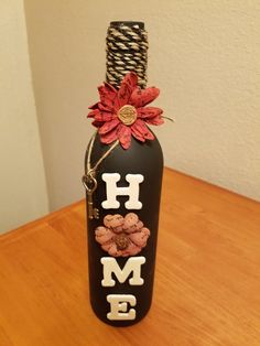 a black bottle with red flowers and the word home painted on it sitting on a wooden table