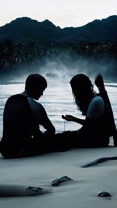 two people sitting on the beach looking at their cell phones