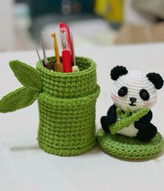 a small crocheted panda bear sitting next to a green cup with toothbrushes in it