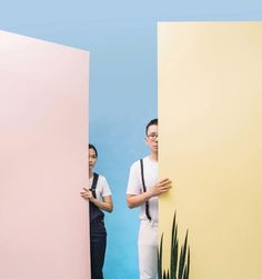 two people are standing in front of large pink and yellow walls, one is holding the other's hand