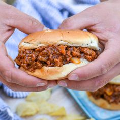 a person holding a sloppy joe sandwich in their hands