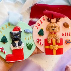 two christmas ornaments are shown in the palm of someone's hand, one has a cat and dog on it