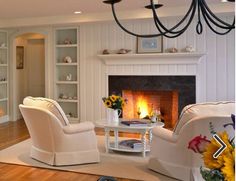 a living room filled with furniture and a fire place under a chandelier in front of a fireplace