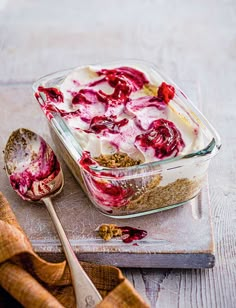 a dessert in a glass dish with strawberries on top and spoon next to it