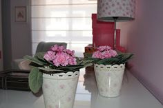 two white vases with pink flowers sitting on a table in front of a lamp