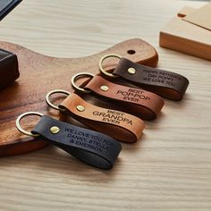 four personalized leather keychains with engraved names on them sitting on a wooden table