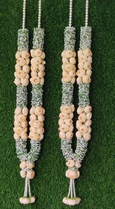 two necklaces made out of beads and flowers on green grass with pearls attached to them