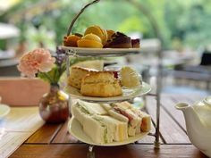 three tiered trays filled with sandwiches and pastries on top of a wooden table