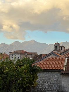 an old building with mountains in the back ground and clouds in the sky above it