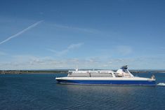 a large white and blue boat in the middle of the ocean on a sunny day