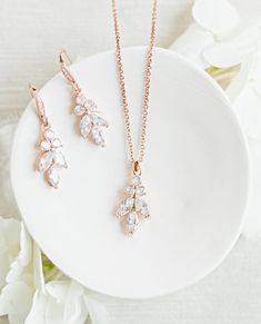 three pieces of jewelry sitting on top of a white plate with flowers in the background