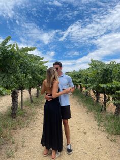 a man and woman are standing in the middle of an empty vineyard with blue skies above them