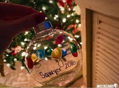 a hand holding a glass ornament that says sawer 2012 with lights on it