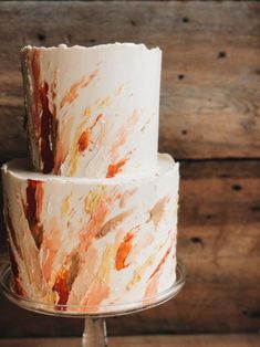 a three tiered cake with orange and white icing on a metal stand in front of wood planks