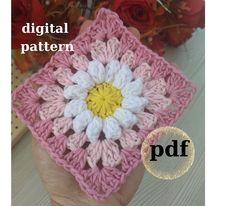 a hand holding a pink and white crocheted square with a yellow center in the middle