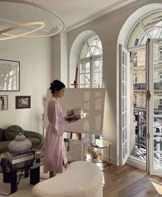 a woman in a pink robe is holding a piece of paper and looking out the window