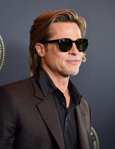 the man in sunglasses is wearing a suit and black shirt with his hair pulled back