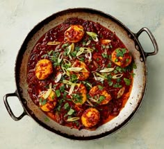 a skillet filled with food on top of a white countertop next to a knife and fork