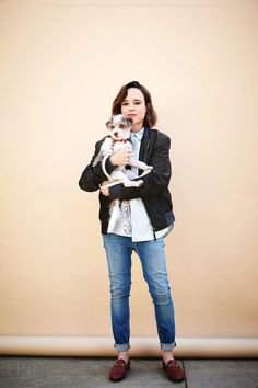 a woman is holding a small dog in her arms and posing for the camera while standing against a wall