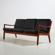 a black leather couch sitting on top of a hard wood frame floor next to a white wall