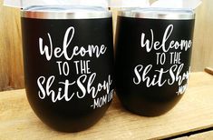 two black tumblers with white lettering are sitting on a wooden table next to each other