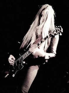 a woman with long blonde hair playing a guitar in front of a microphone on stage