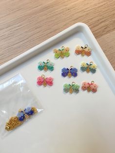 a tray with six different colored beads on it and one is in the shape of a butterfly