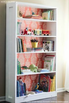 a bookshelf filled with lots of books next to a wallpapered wall