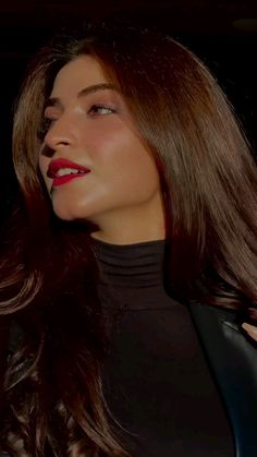 a woman with long brown hair wearing a black top and red lipstick looking off to the side