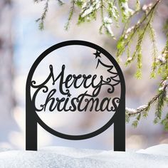 a merry christmas sign hanging from the side of a snow covered pine tree in front of a snowy background