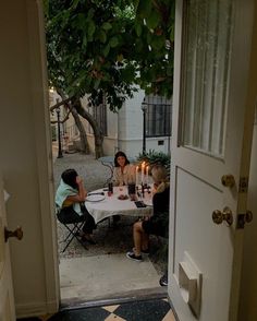 two women sitting at a table with candles in front of them and another woman standing by the door