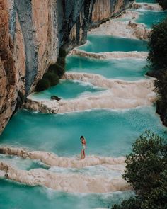 a woman standing on the edge of a cliff next to blue water and rocky cliffs