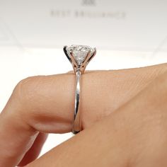 a woman's hand holding a diamond ring on her finger, with the center stone in