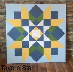 a quilted wall hanging on the side of a brick wall with blue, yellow and green squares