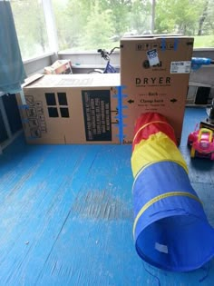 a blue and yellow tube sitting on top of a wooden floor next to a cardboard box