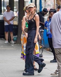 a woman walking down the street with a hat on her head and people standing around