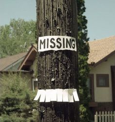 a missing sign on a telephone pole in front of a house with trees and houses behind it