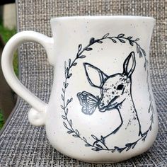 a white coffee cup with a deer on it's side sitting on a chair