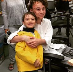 a woman sitting next to a young boy in a barber chair with blood all over his face