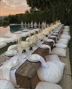 a long table is set up with white plates and place settings for an outdoor dinner