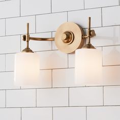 a bathroom light with three lights on the wall and white tiled walls behind it,