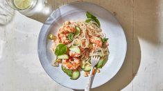 a white plate topped with pasta and shrimp next to a glass of water on top of a wooden table