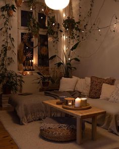 a living room filled with lots of furniture and plants on the wall above it is a coffee table surrounded by candles