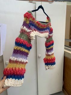 a hand holding up a multicolored knitted scarf hanging from a hook on a white door